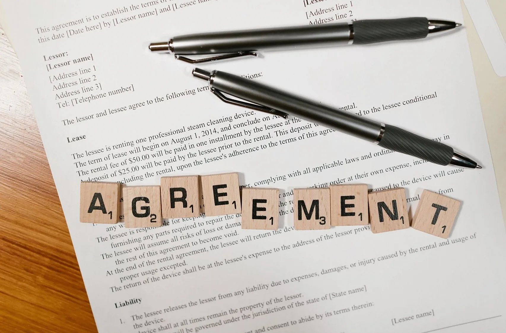 契約書の上に置かれた2本のペンと「AGREEMENT」の文字タイル